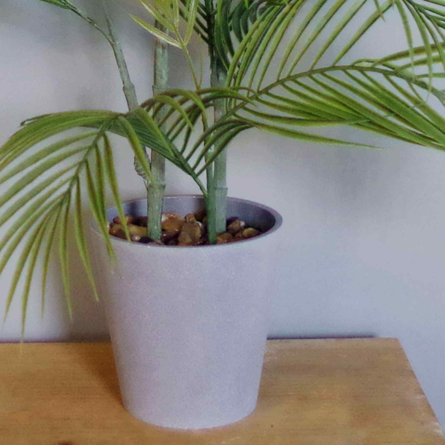 Close‑up of grey decorative planter with artificial palm stems and fixed pebbles.