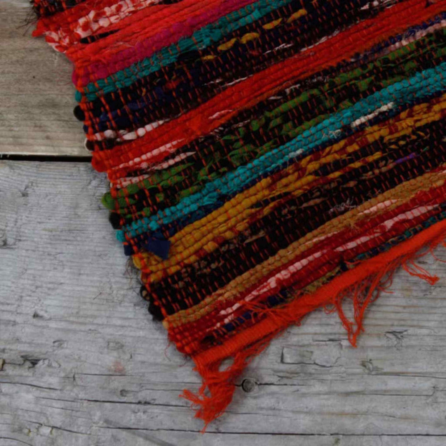 Corner detail of orange striped rag rug on wooden floor, highlighting fringe and fabric texture.