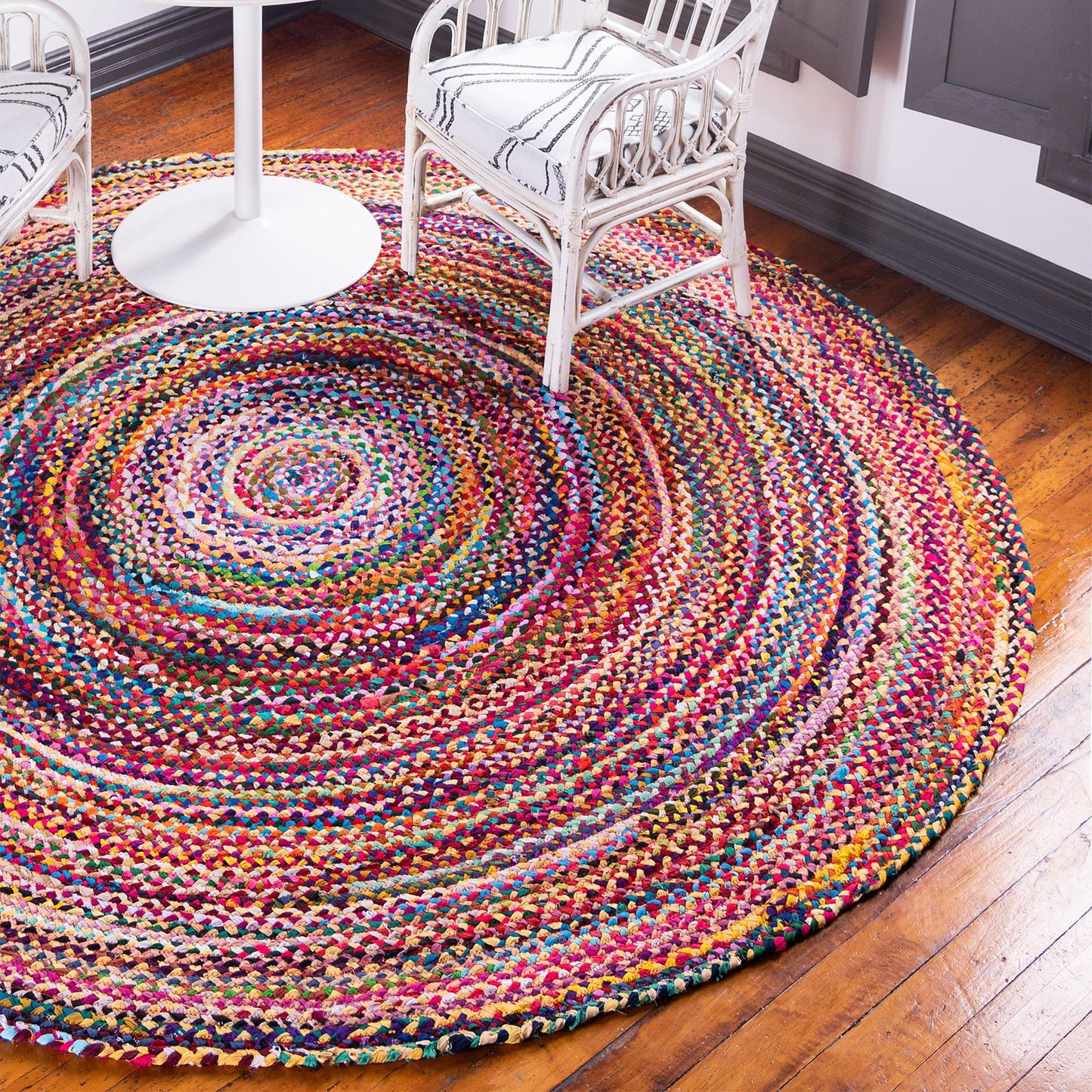 A round jute and cotton rug placed under a white wire-frame chair on a wooden floor.