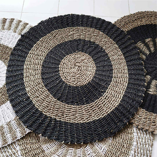 Round black and tan seagrass rug, 1m diameter, handwoven circular design, styled next to other natural rugs.