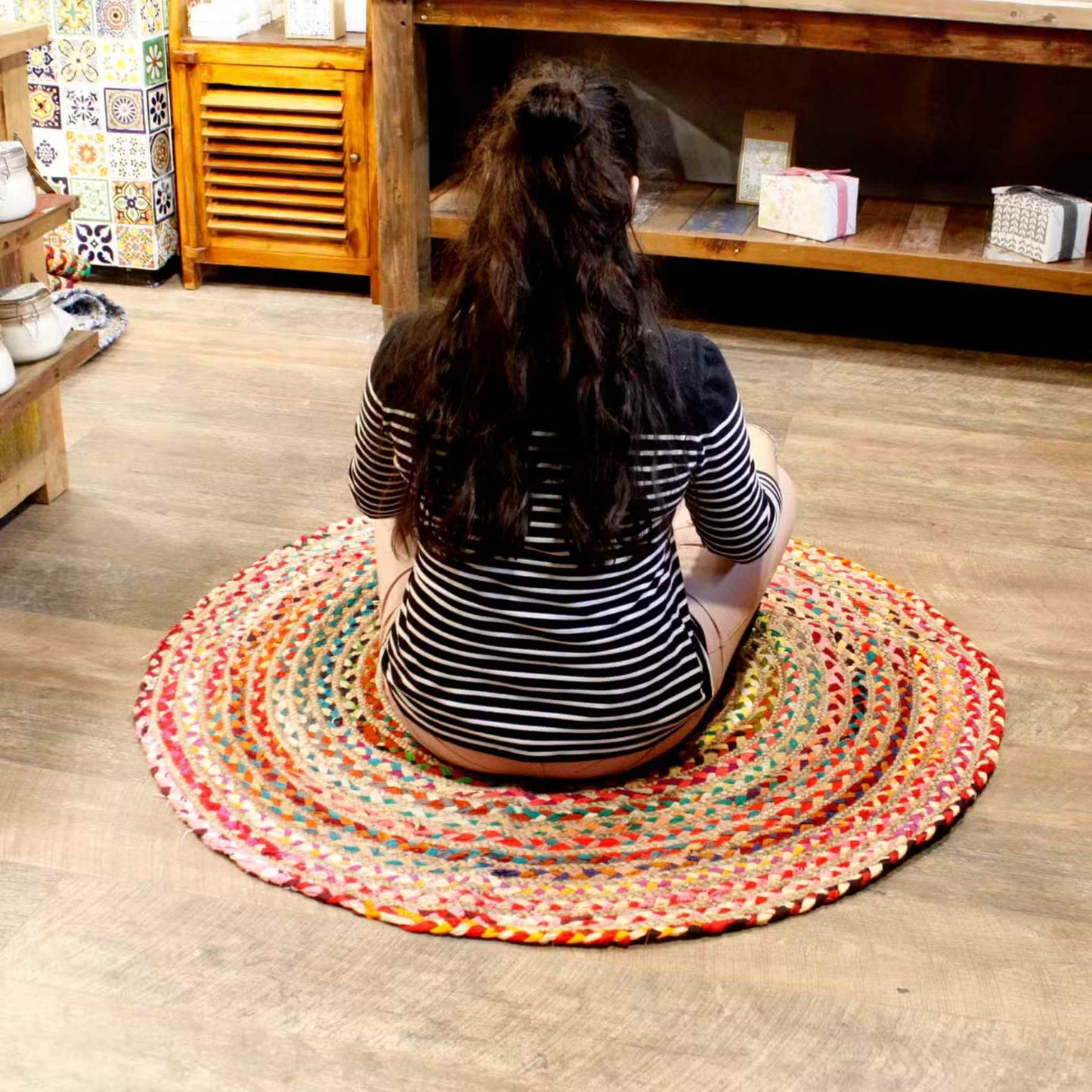 Woman sitting on a round jute and recycled cotton rug in a cosy wooden-floored room.