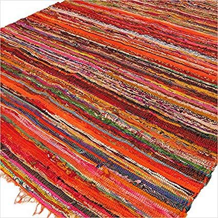 Angled view of an orange handmade cotton rag rug with layered stripes in reds, pinks, and purples.