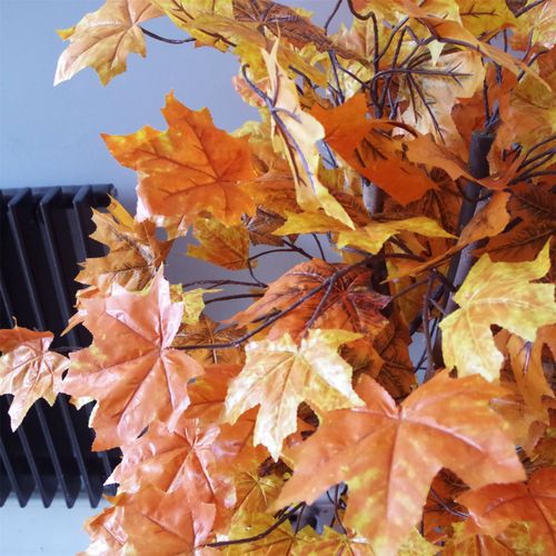 Close-up of realistic orange maple leaves on artificial tree.