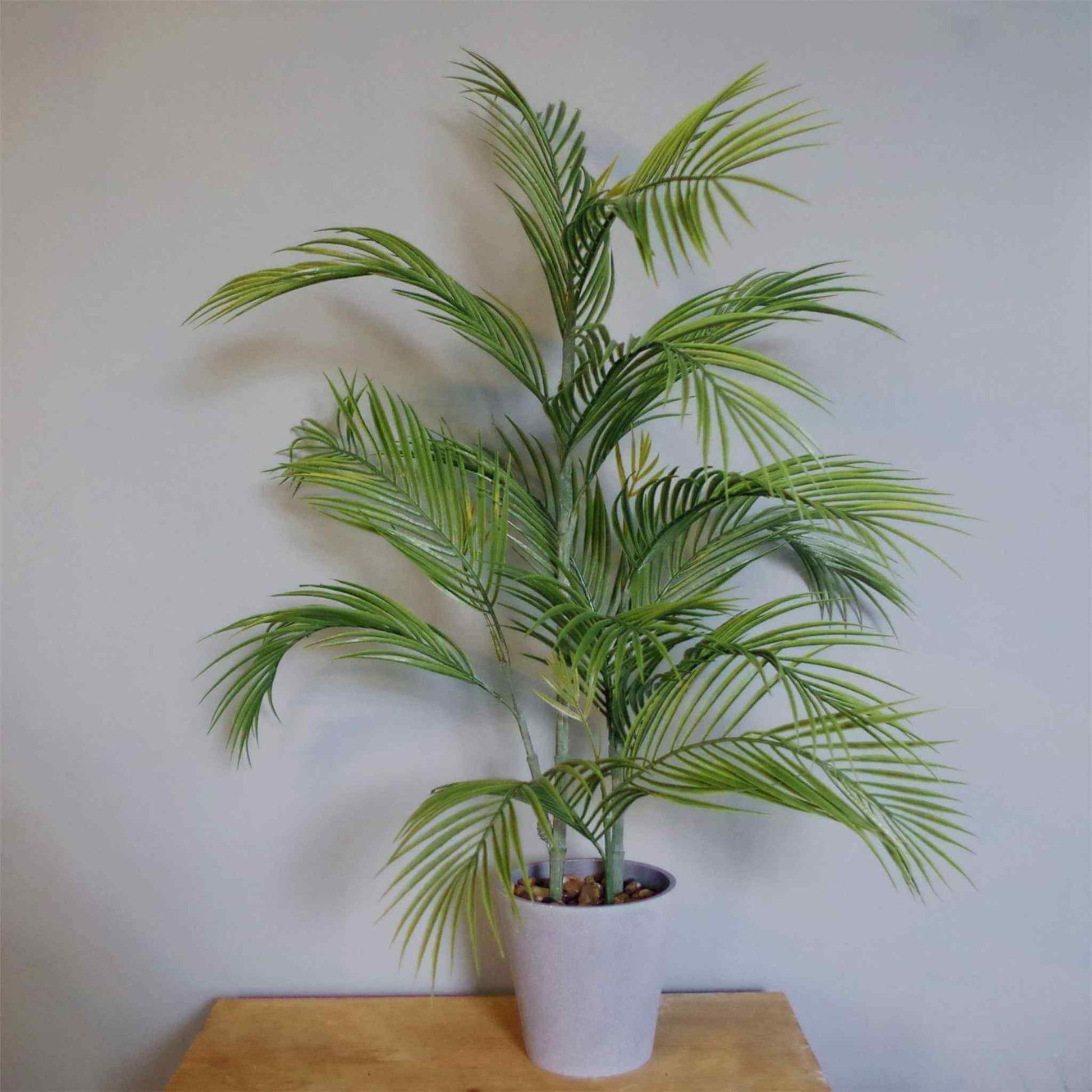 Artificial 90cm palm tree in grey planter on a wooden table, green leaves against a neutral wall.