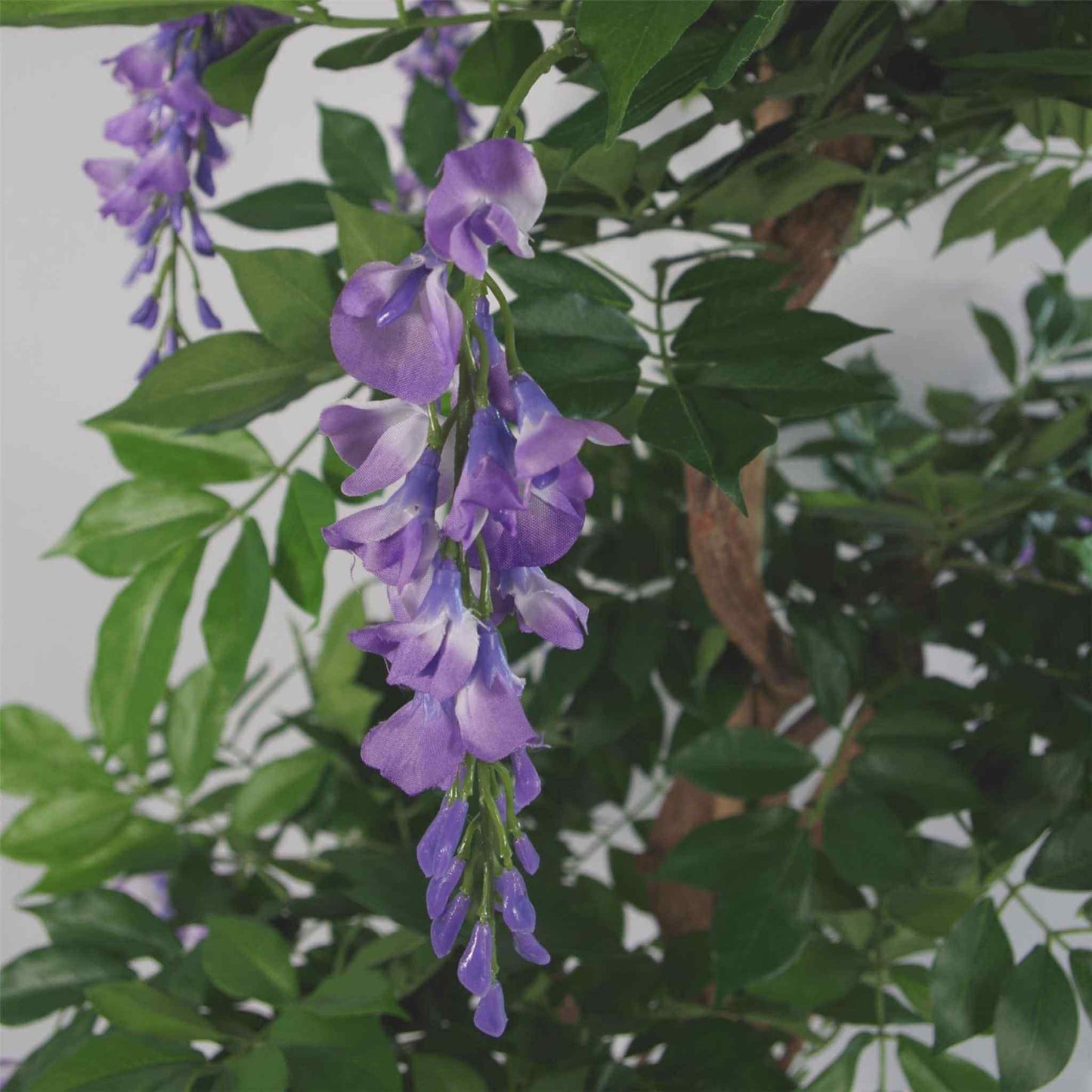 Close-up of a realistic artificial wisteria flower cluster with soft purple petals and green leaves.
