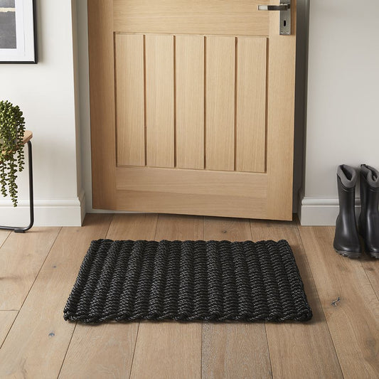 Charcoal braided doormat placed at a wooden front door with boots beside.