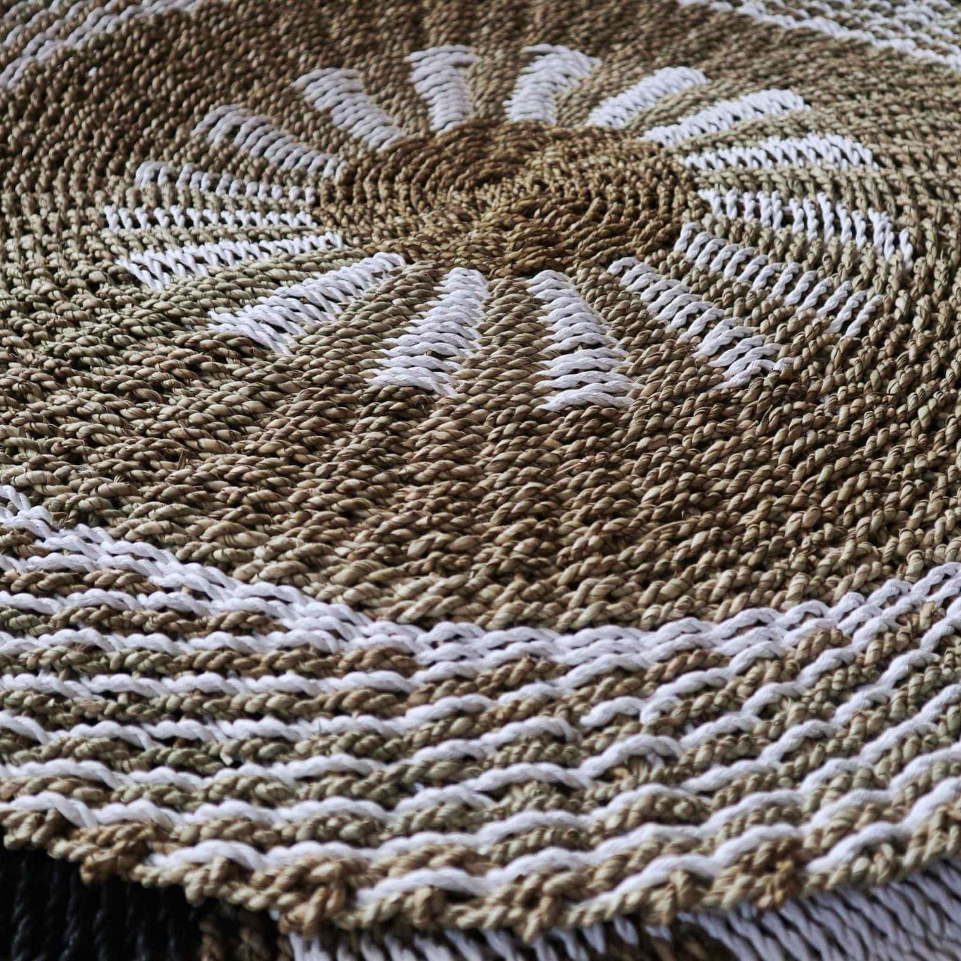 Detailed close-up of handwoven seagrass fibres in natural tan and white sunburst pattern, showing rich woven texture.