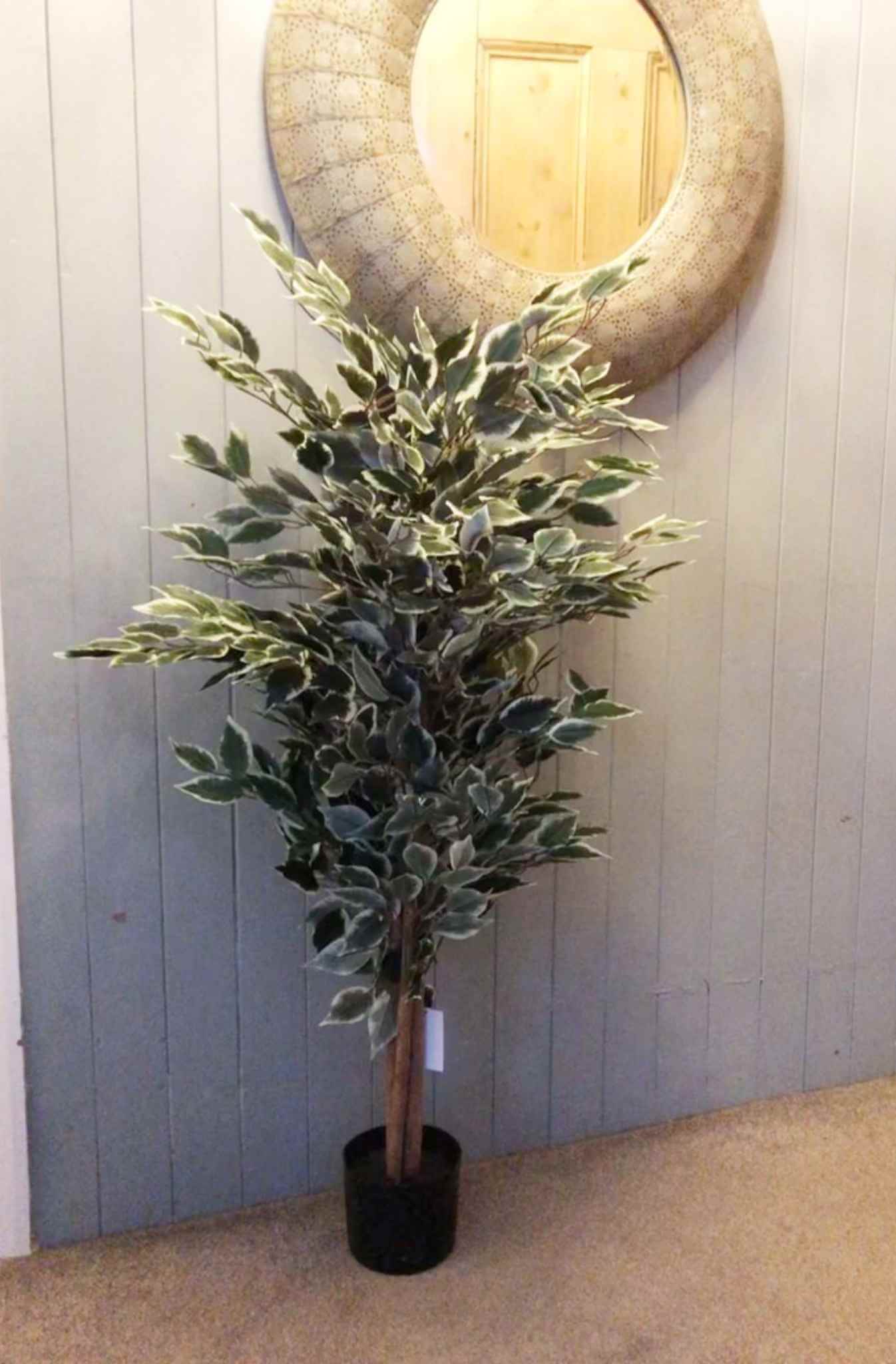 Artificial ficus tree styled in a carpeted hallway with a round wall mirror.