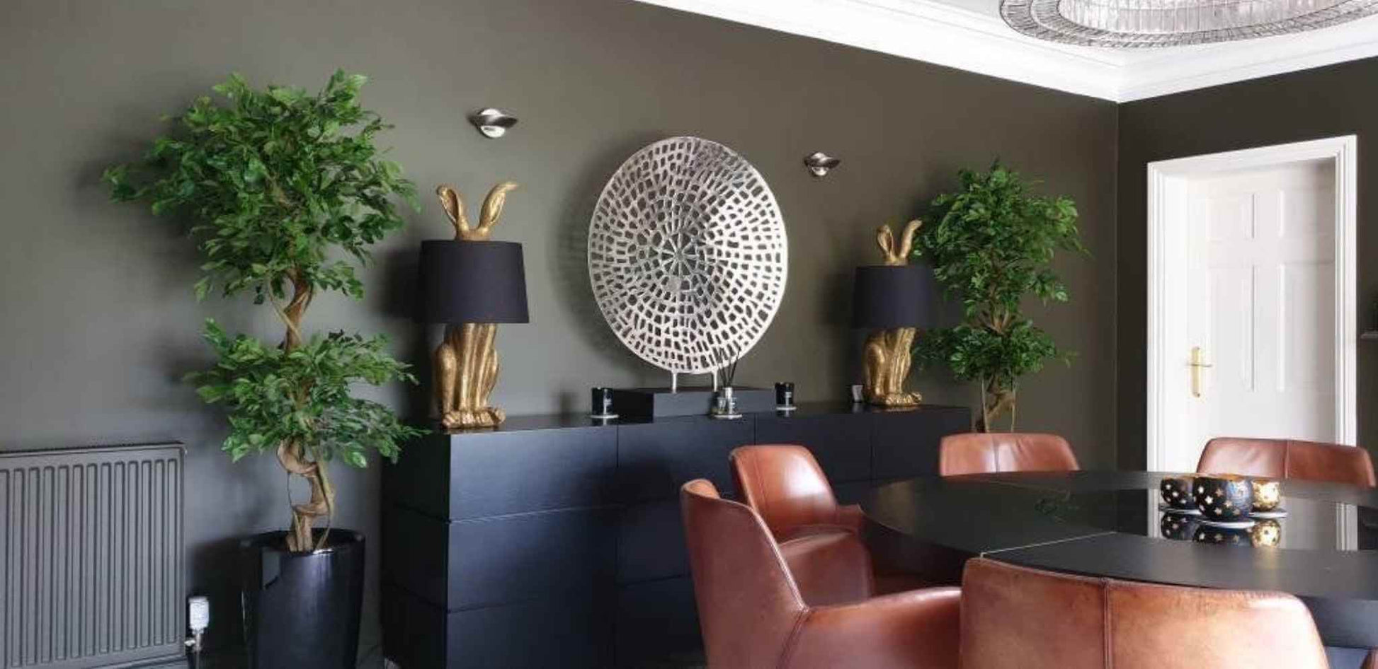 Two 150cm artificial ficus trees in a modern dining space with brown leather chairs and black furniture.