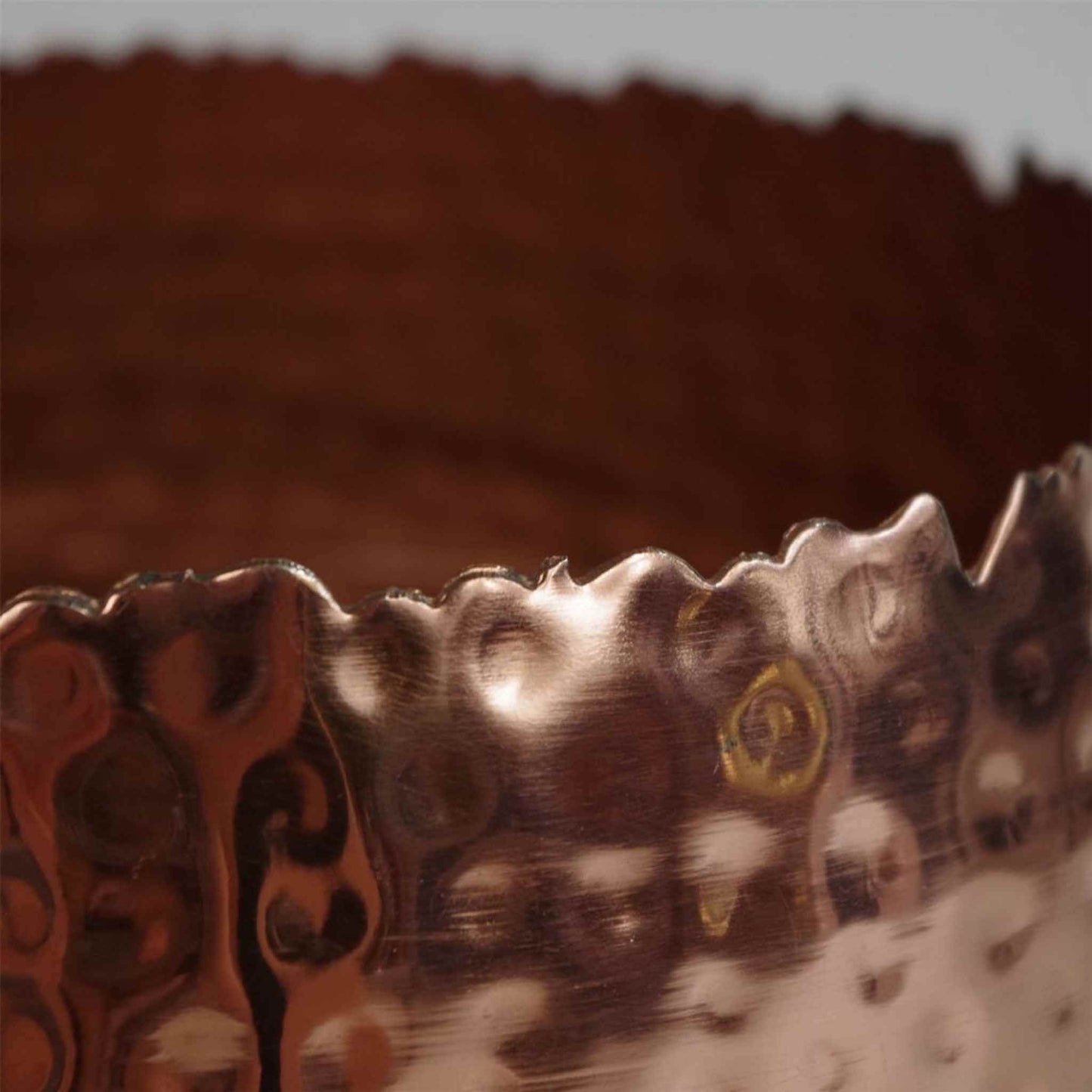 Close-up detail of a hammered copper metal planter rim, highlighting the handcrafted curvy edge texture.