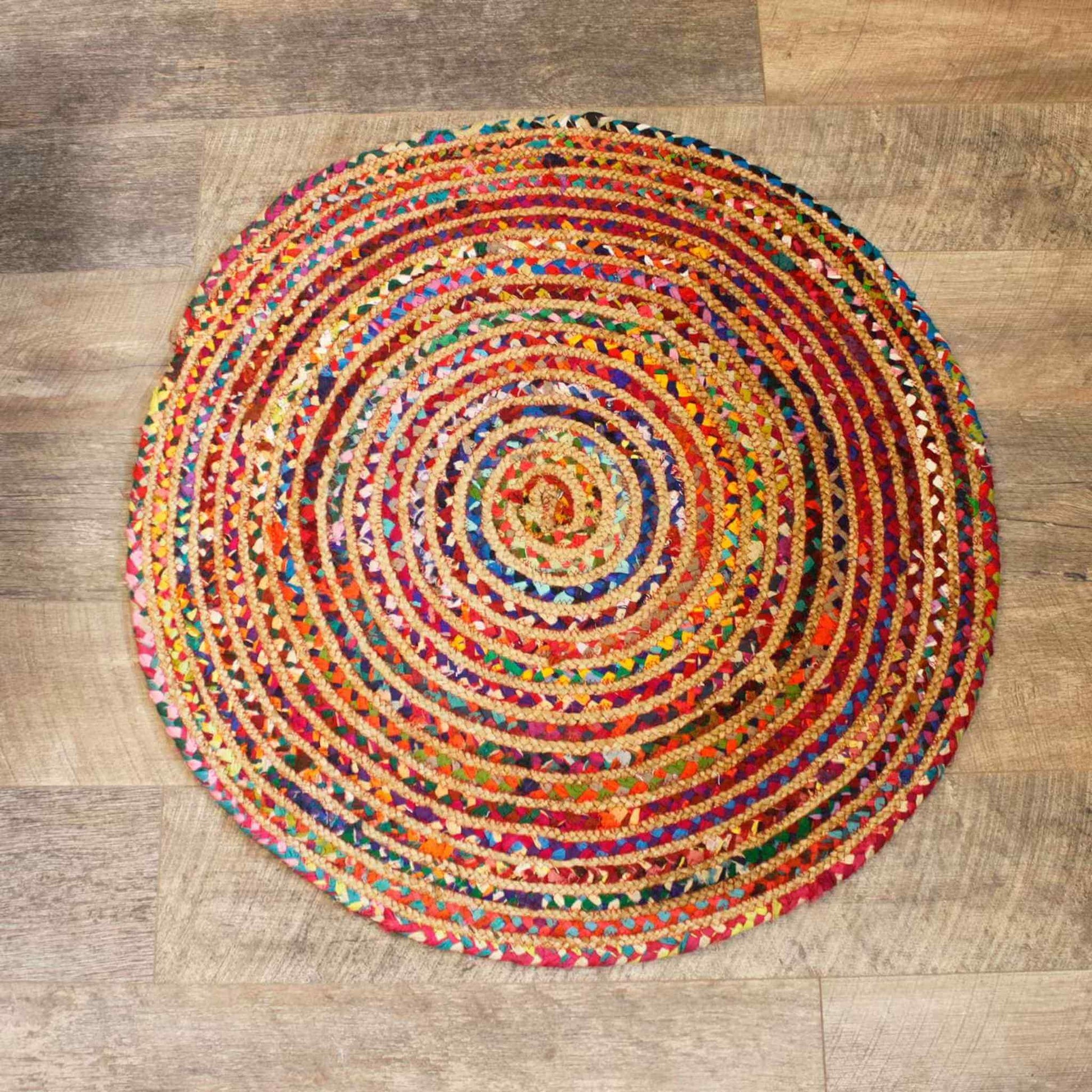 Handcrafted round jute and cotton rug in bright mixed colours, photographed from above on a rustic wooden floor.