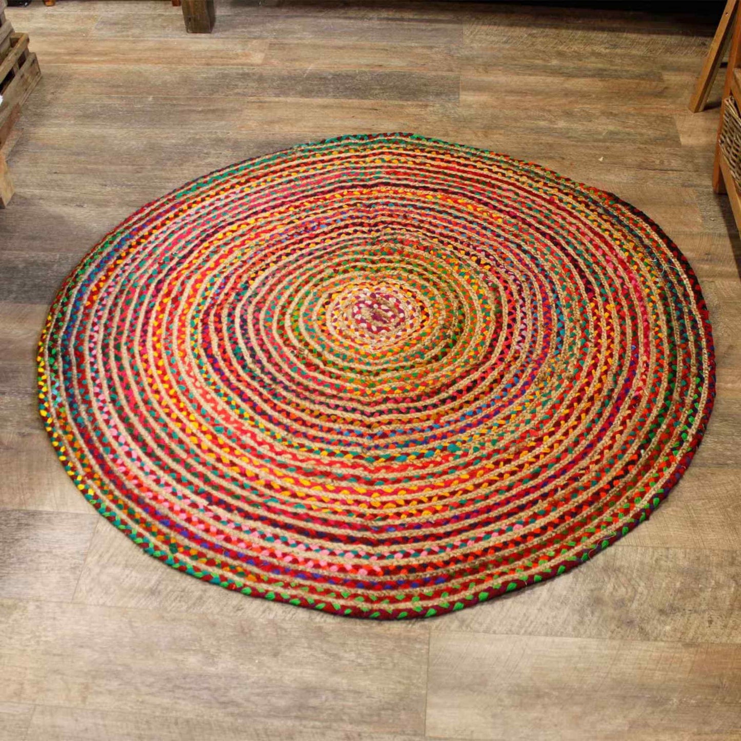 Close view of a round jute and recycled cotton rug on a wooden floor, highlighting its hand‑woven texture and mixed bright colours.
