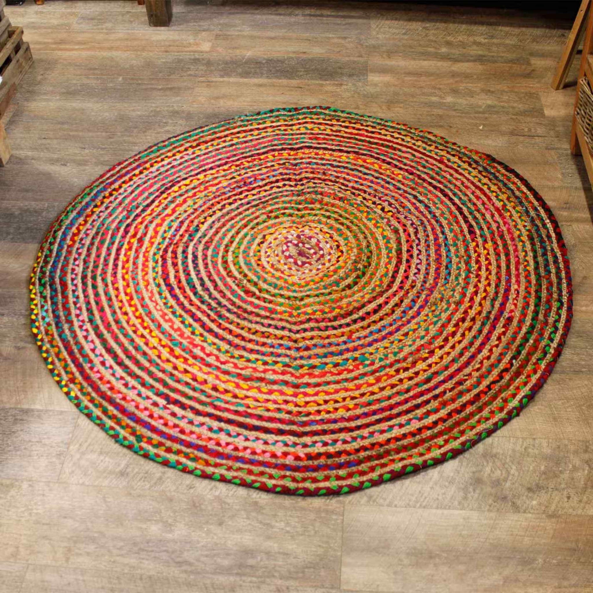 Close view of a round jute and recycled cotton rug on a wooden floor, highlighting its hand‑woven texture and mixed bright colours.