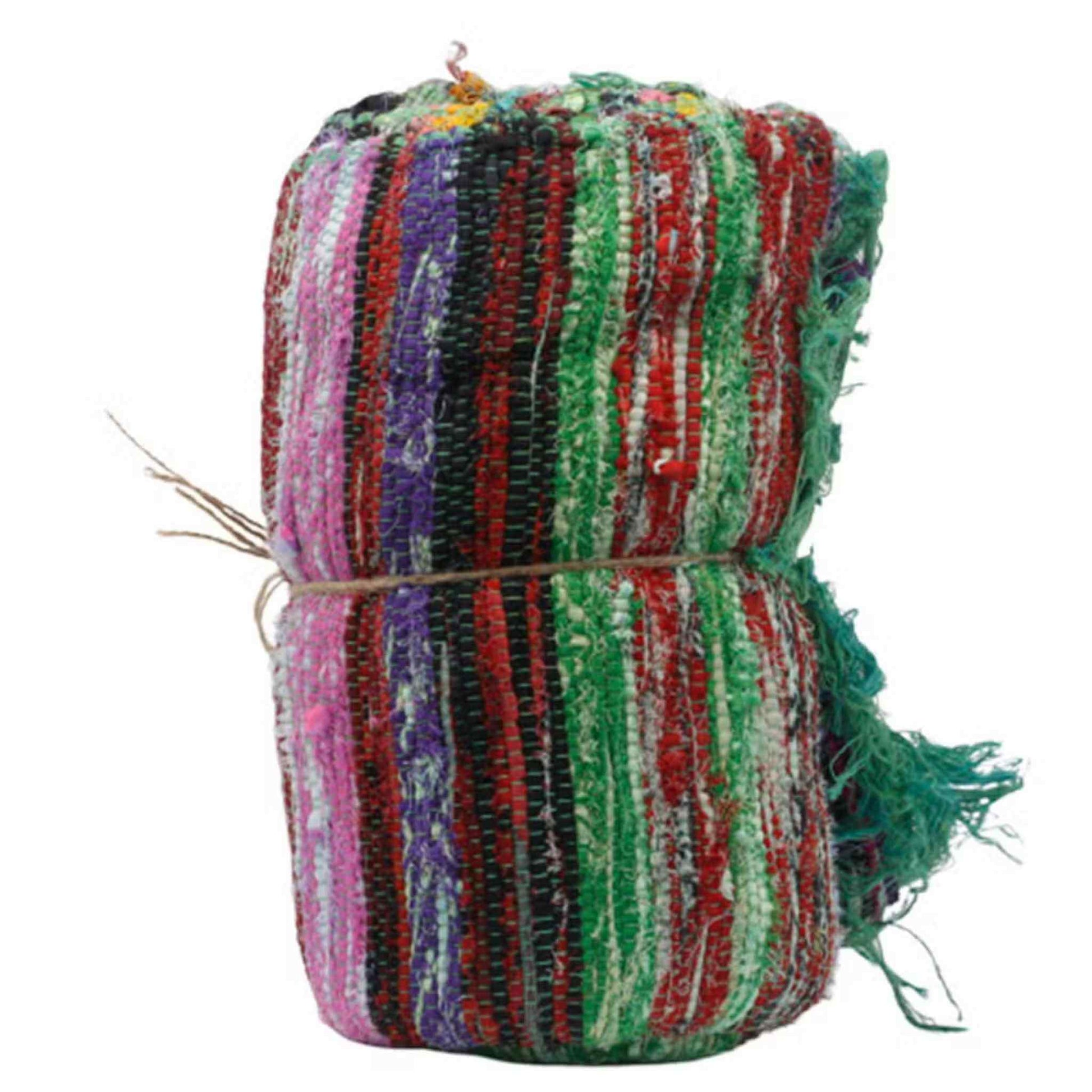 Rolled luxury Indian rag rug with multicoloured stripes and a green fringe tied with twine.