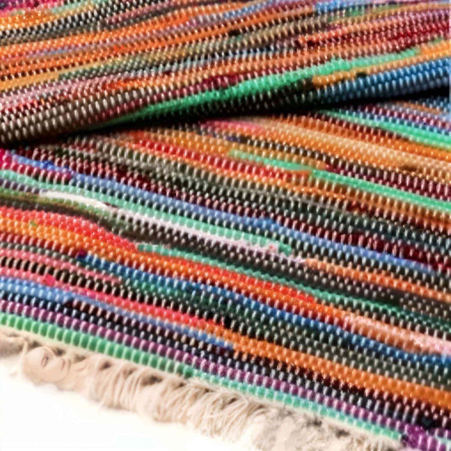 Detail view of a woven cotton rag rug showing colourful horizontal stripes and fringed edge.