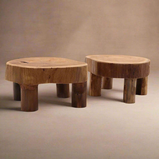 Pair of low round teak display stands on a beige background, highlighting natural wood grain and cylindrical legs.