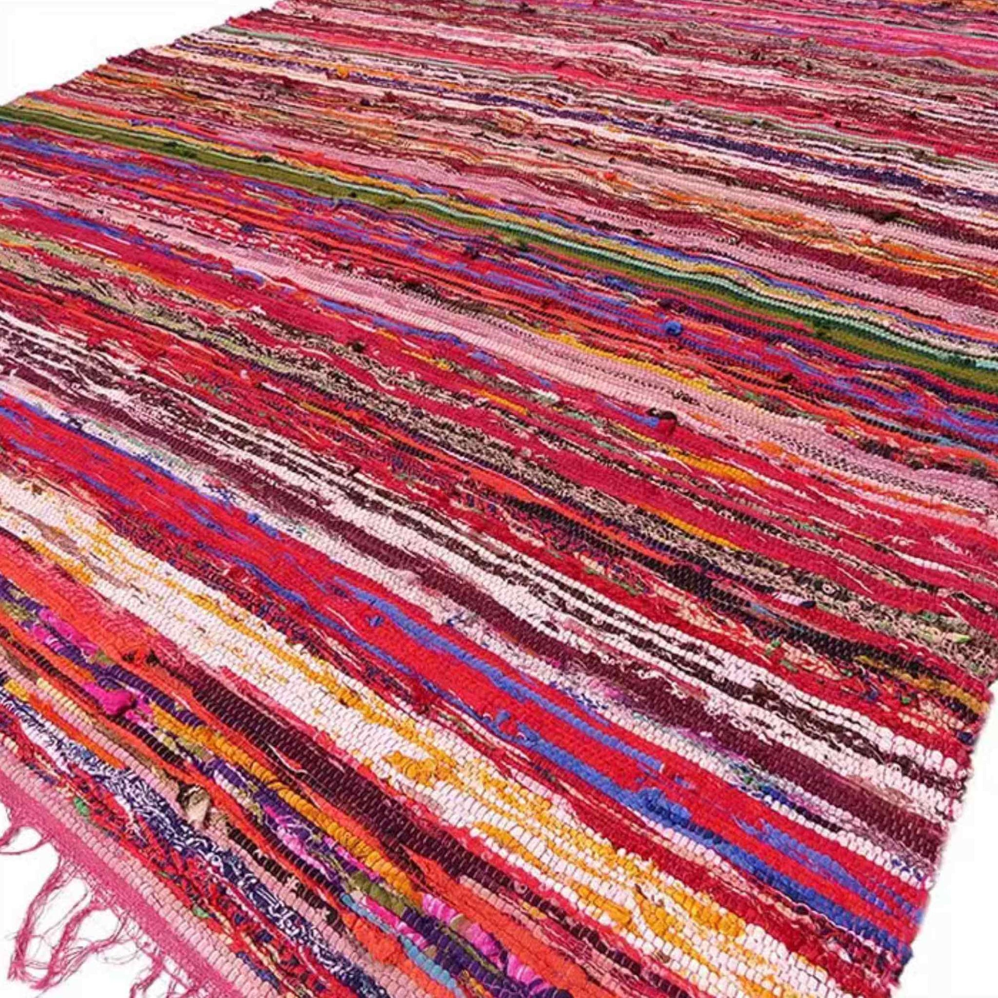 Luxury red Indian rag rug in multicoloured stripes laid flat on the floor, showing woven cotton texture and red fringe edges.
