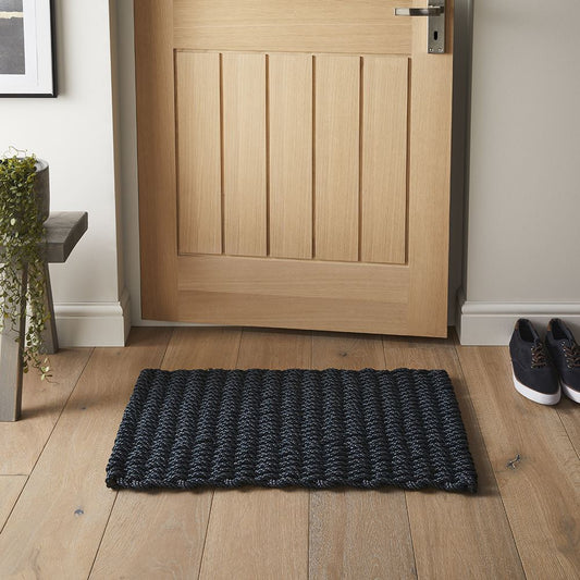 Navy braided polypropylene doormat placed at a wooden front door entrance.