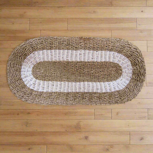 White and tan oval seagrass rug, 60x120cm, placed on natural wooden flooring.