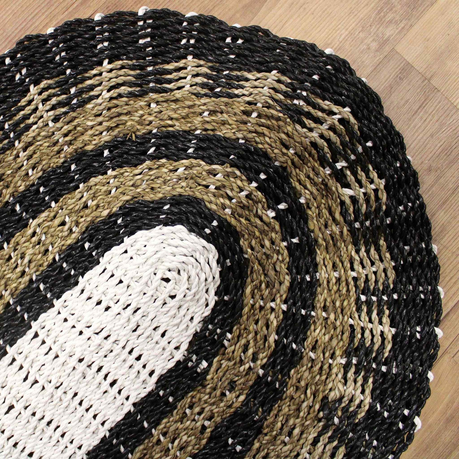 Close-up detail of woven seagrass rug showing braided oval pattern in black, white and tan.