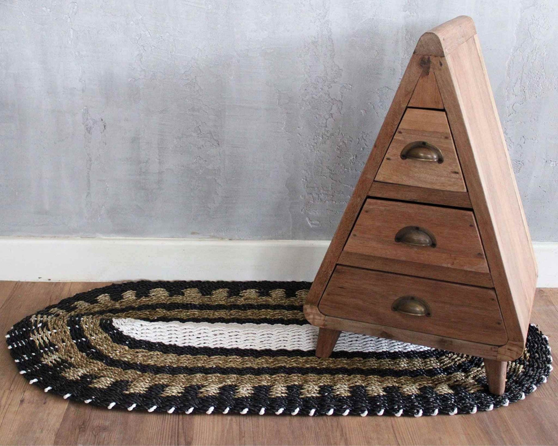 Oval seagrass rug in black, white and tan, 60x120cm, styled beneath a small wooden drawer unit on wooden flooring.