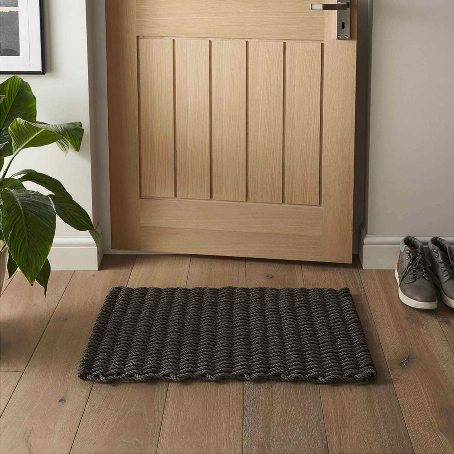 Slate braided polypropylene doormat placed by a light oak door on wooden flooring.