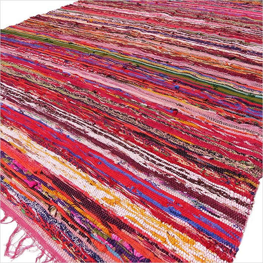 Angled shot of rug laid out with fringe detail and pink, purple, red and orange tones.
