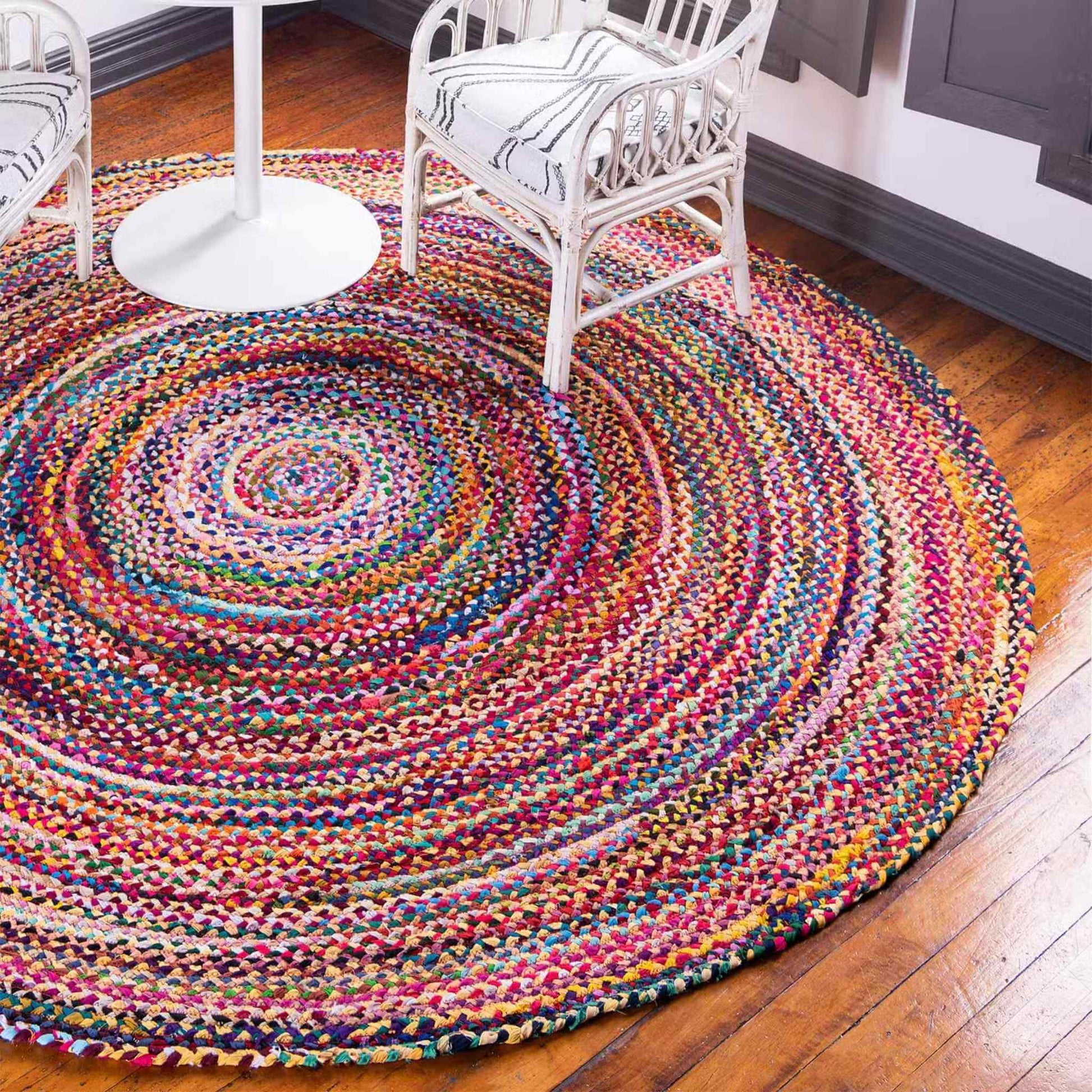 Round jute and recycled cotton rug placed under two white chairs and a small table in a bright room.