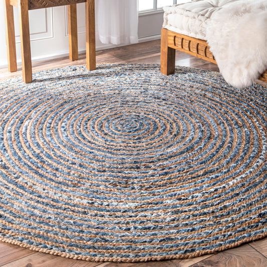 A round jute and recycled denim rug in a light bedroom, set beneath a wooden coffee table and bed.