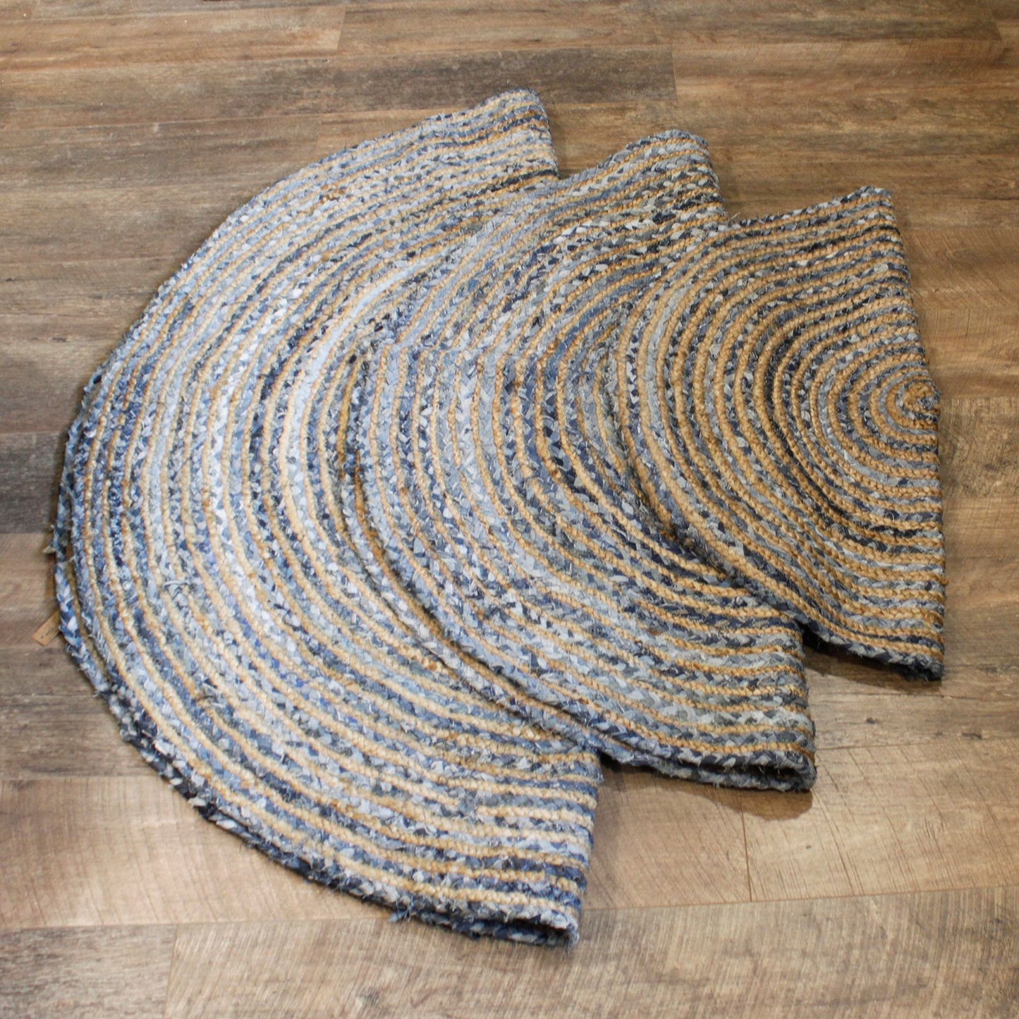 Stack of three round braided jute and denim rugs in increasing sizes.