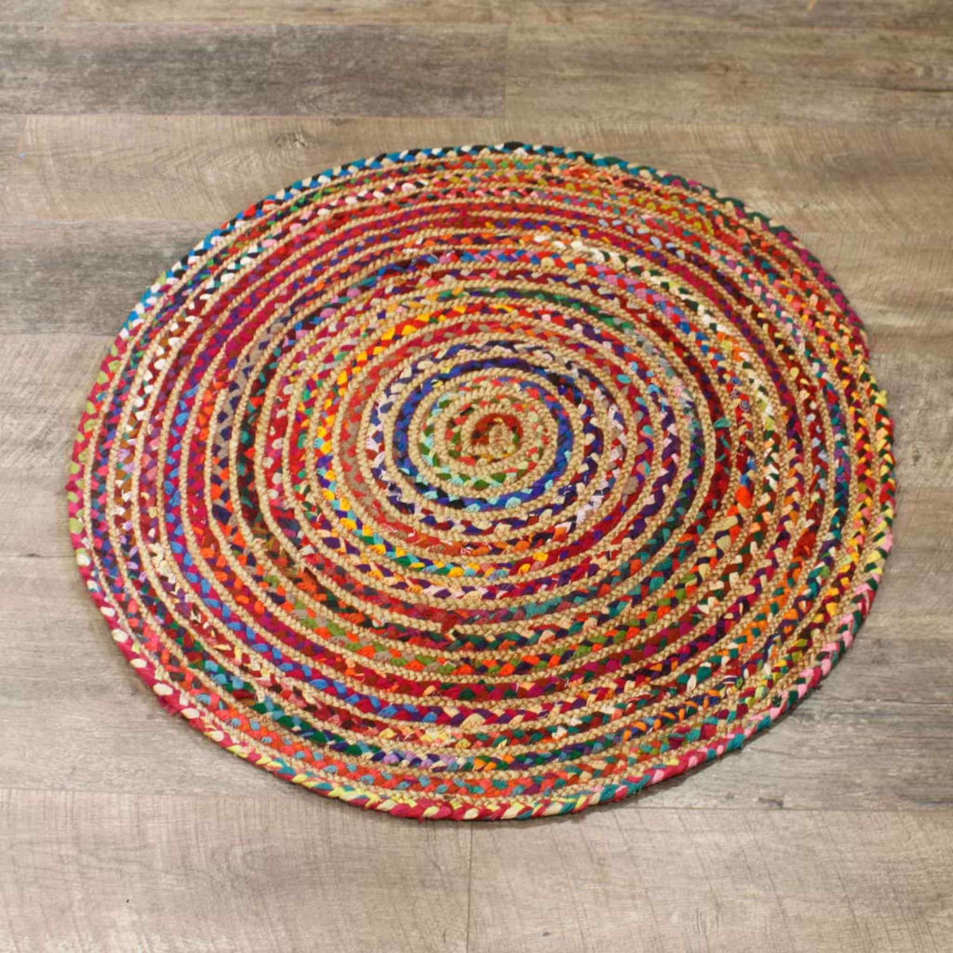 Round 90 cm multicoloured jute and recycled cotton rug on a wooden floor – vibrant concentric braided pattern.