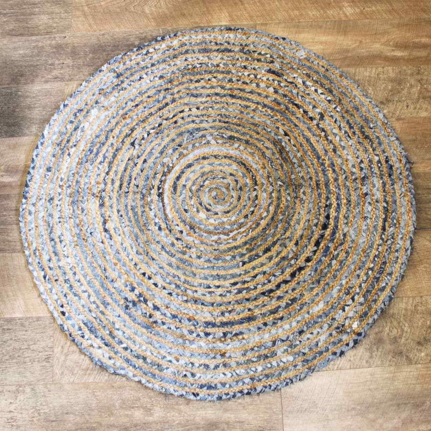 Overhead view of a 120cm round jute and recycled denim rug showing a spiral pattern of blue and beige fibres on a wooden floor.