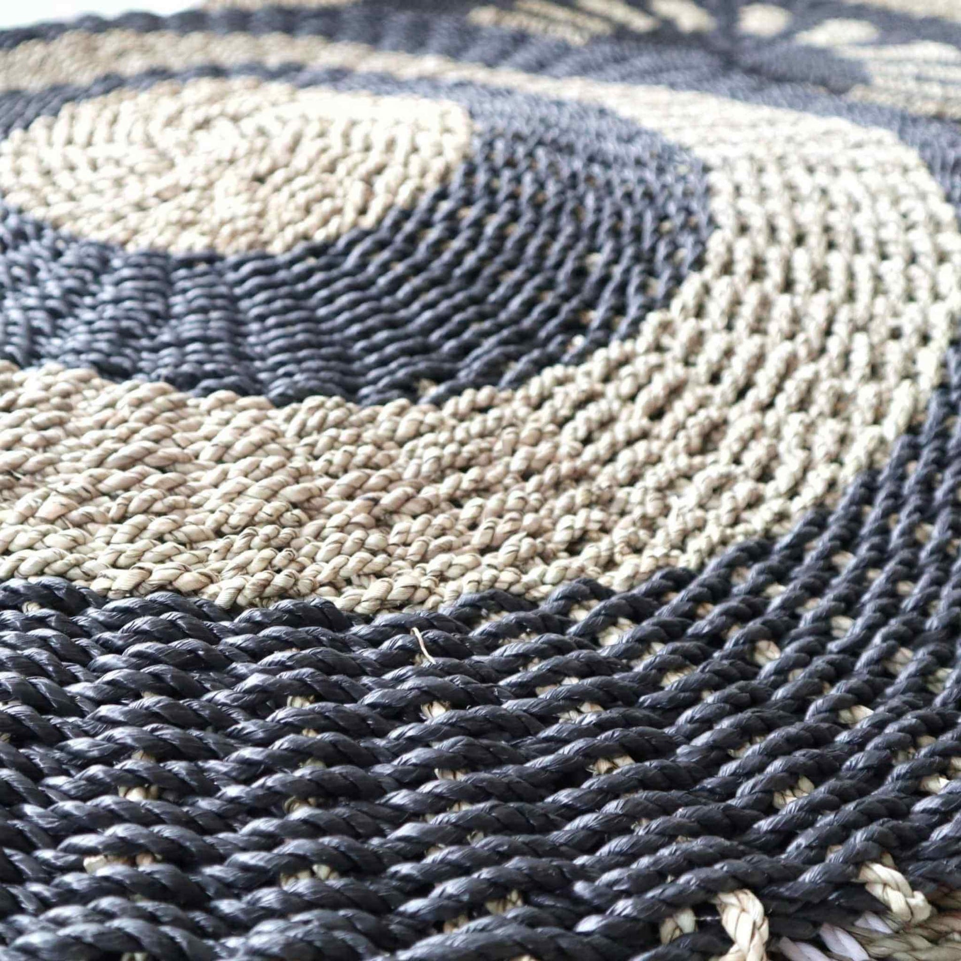 Detail of woven black and tan seagrass rug, showing hand-braided texture and round design.