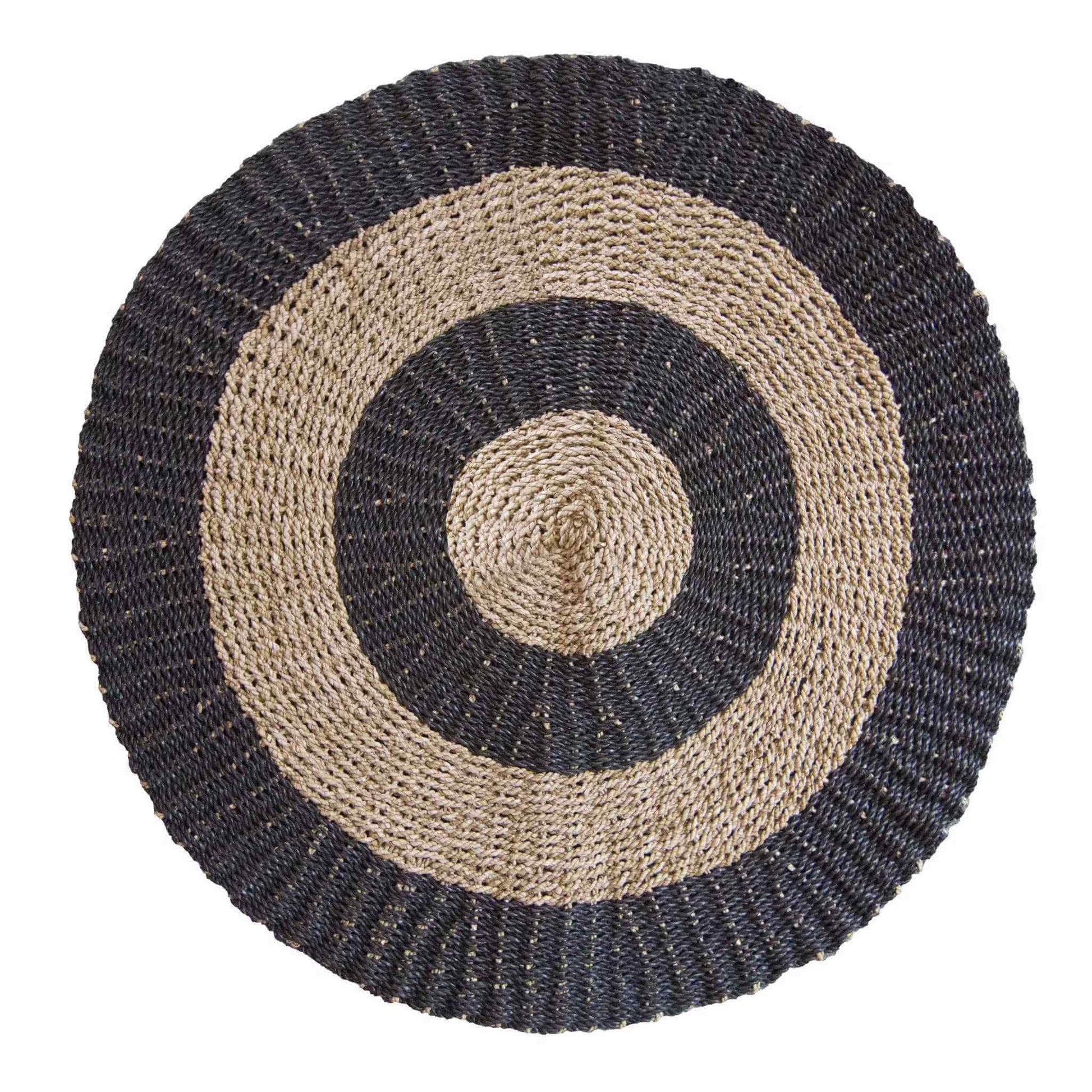 A 1 metre round seagrass rug in black and tan with a bold circular pattern on a white background.