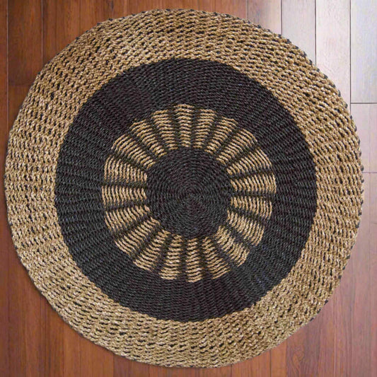Top angle of a round seagrass rug in black and tan on a wooden floor, highlighting its texture.