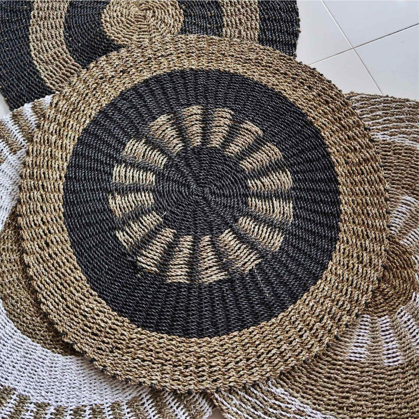 Stack of round seagrass rugs in black, tan, and white, demonstrating various designs.