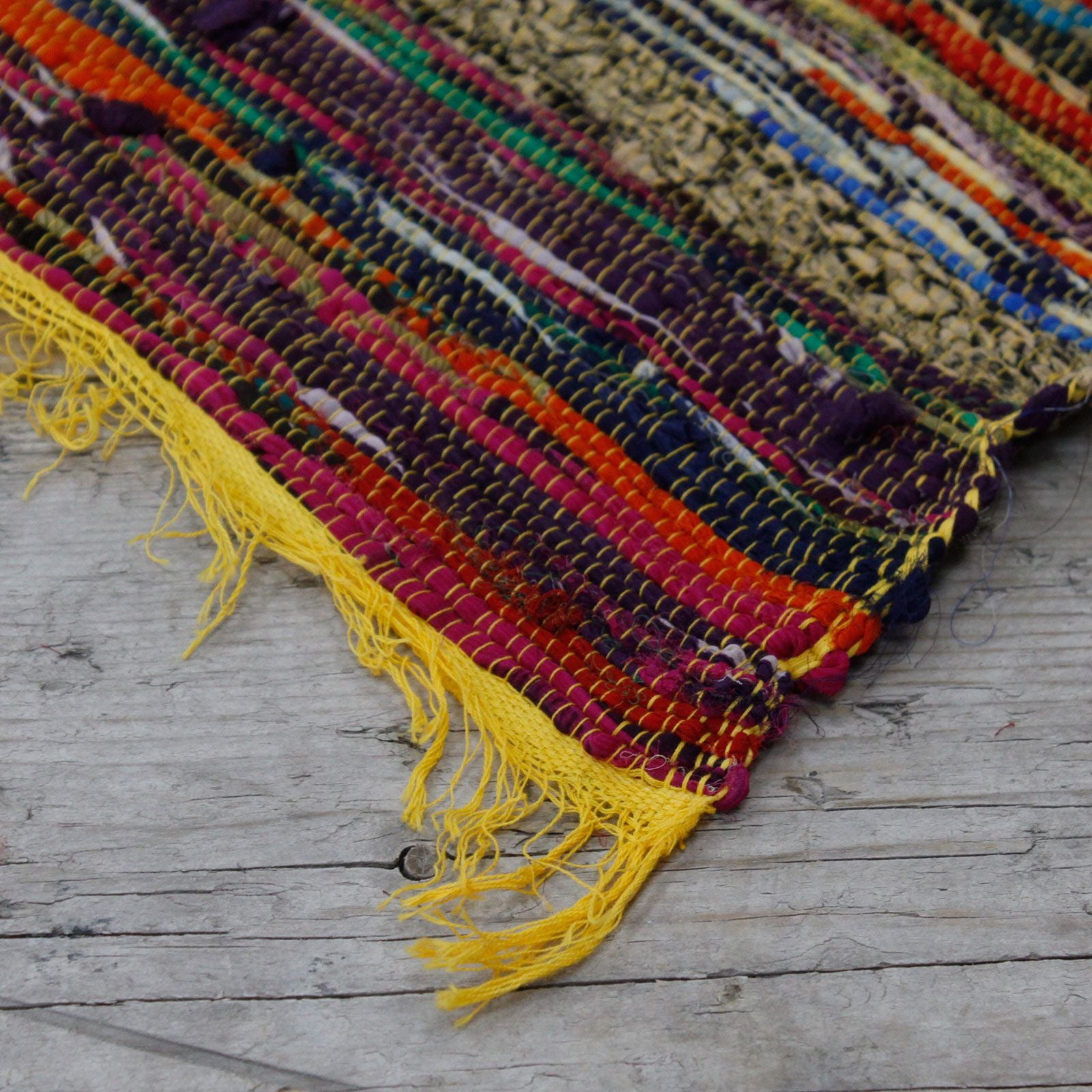 Corner detail of woven rug showing yellow tassels on wooden floor.