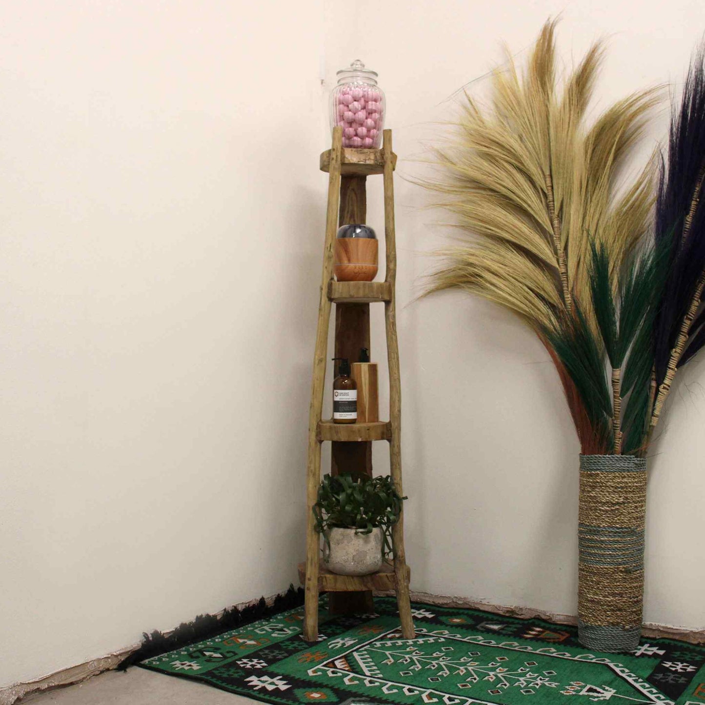 Tall natural teak corner shelving unit styled in a neutral room with plant décor, rug, and accessories on shelves.